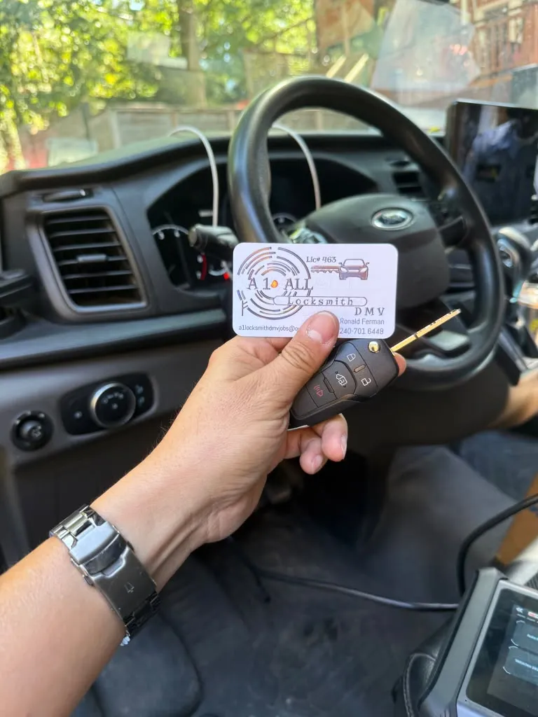 Ford remote key and A1 All Locksmith DMV business card held beside a vehicle steering wheel