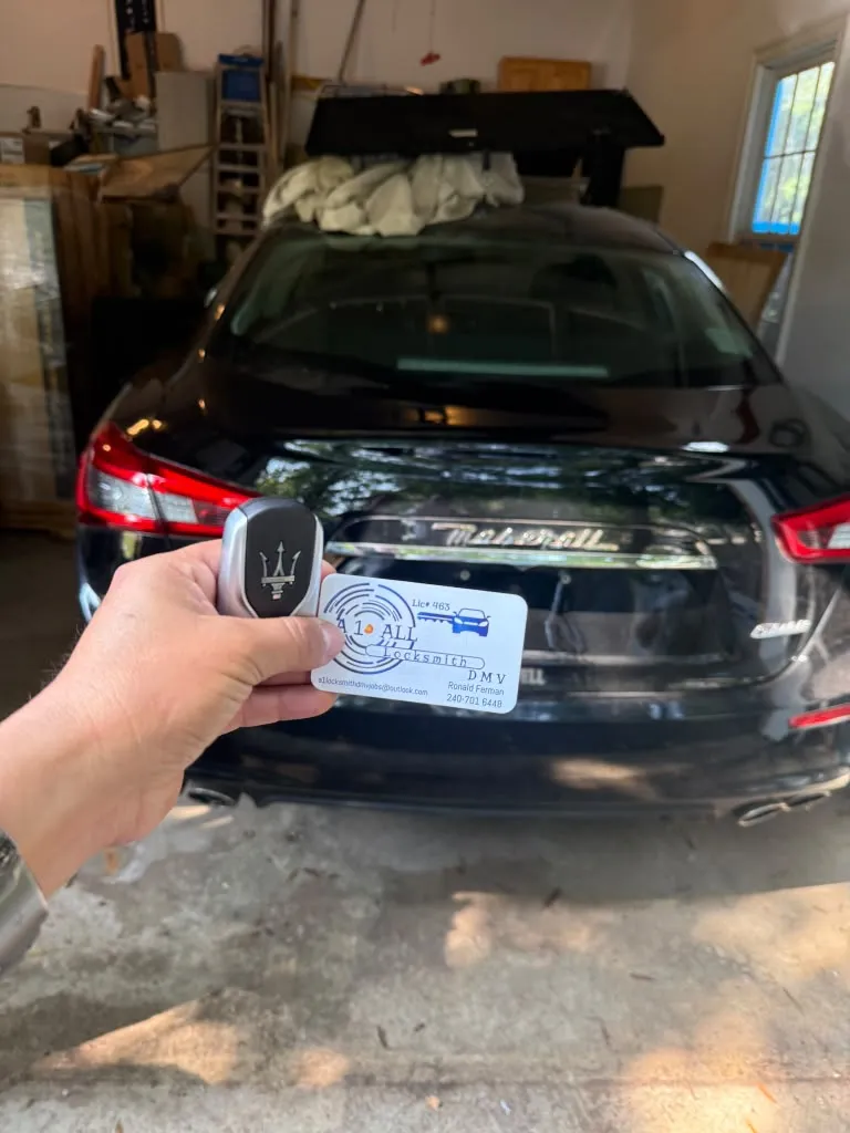 Maserati key fob and A1 All Locksmith DMV business card held behind a black car parked in a garage