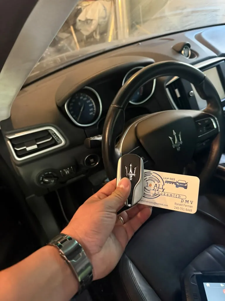 Maserati key fob and A1 All Locksmith DMV business card held in front of the vehicle steering wheel