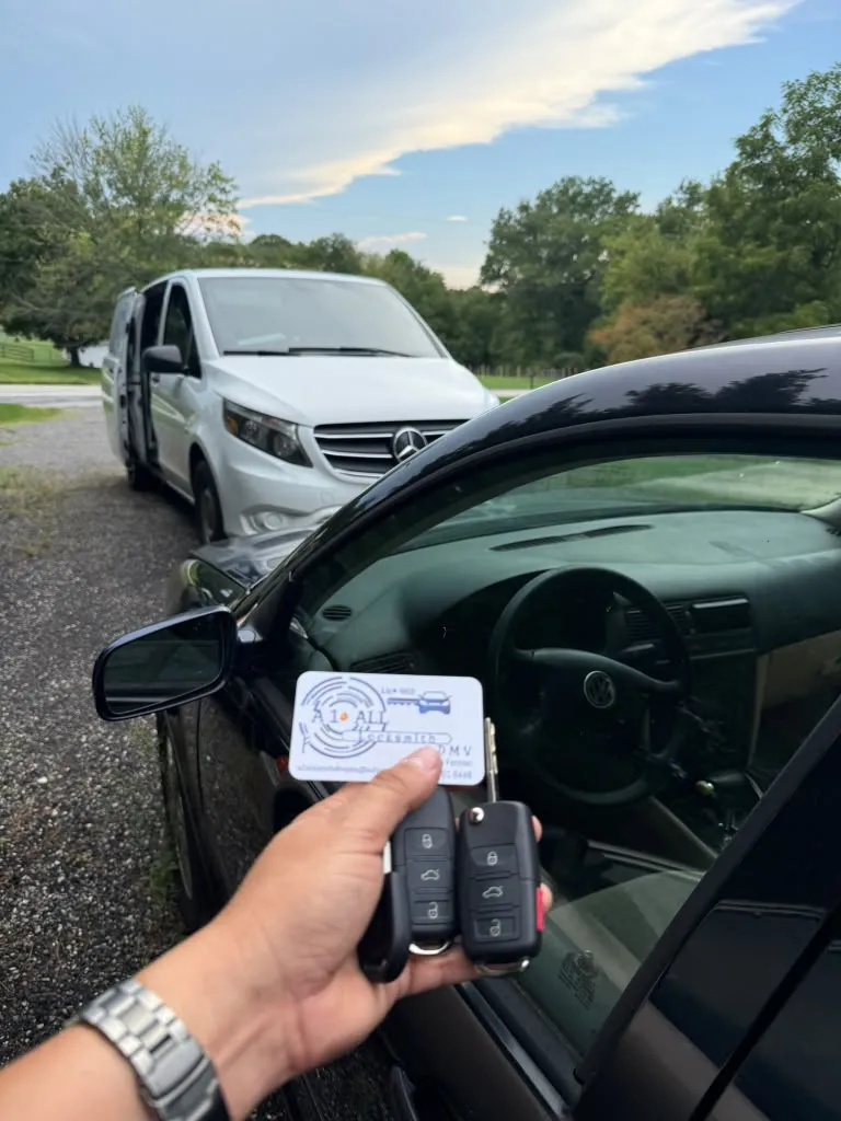 Two remote keys and an A1 All Locksmith DMV card beside an open Volkswagen driver door, with a white van behind