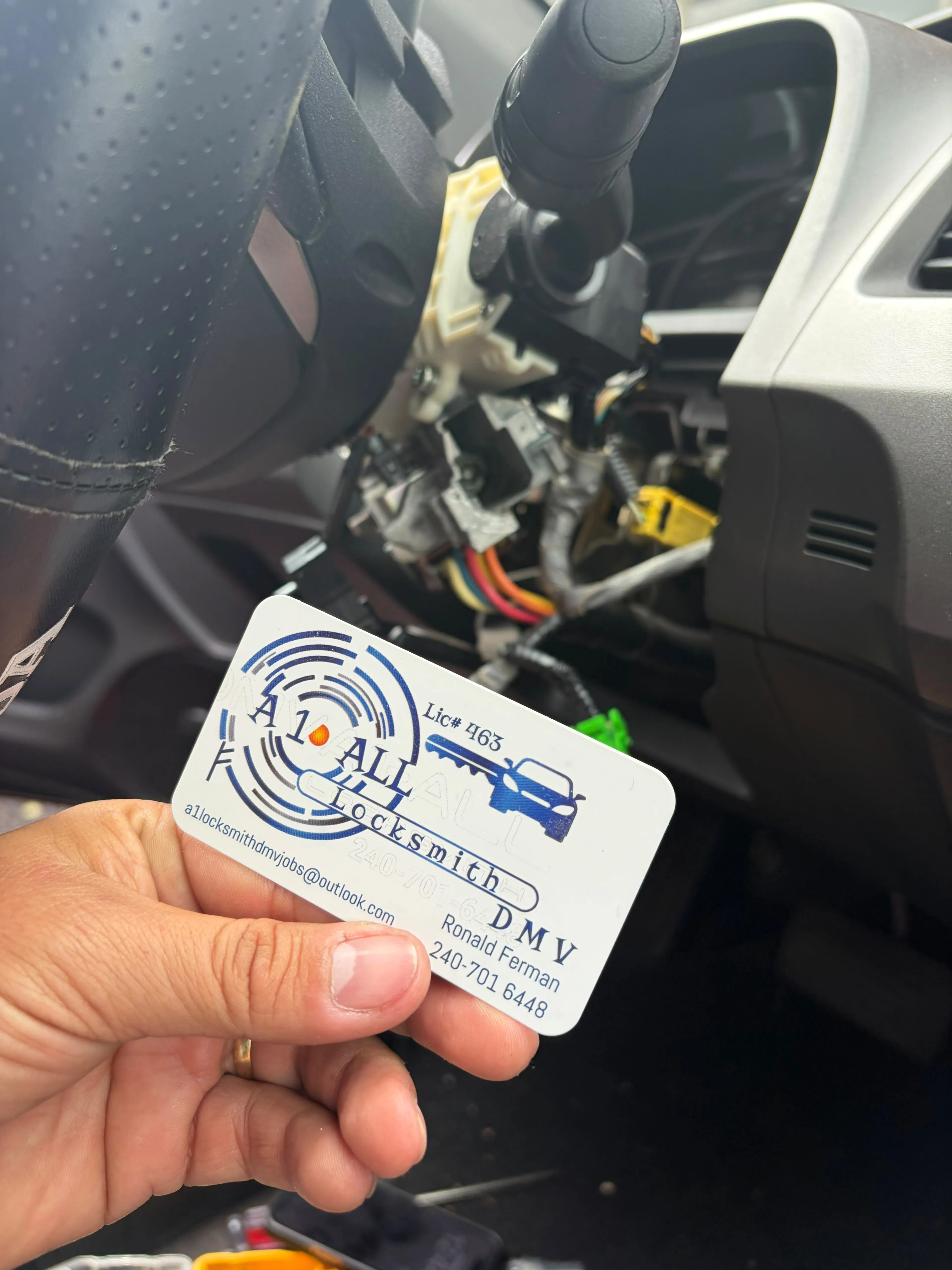 Exposed steering-column components beside an A1 All Locksmith DMV business card