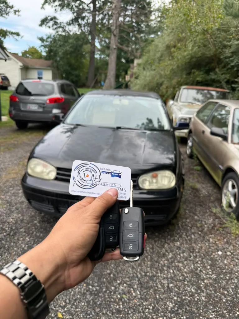 Two remote car keys and an A1 All Locksmith DMV business card held in front of a black Volkswagen
